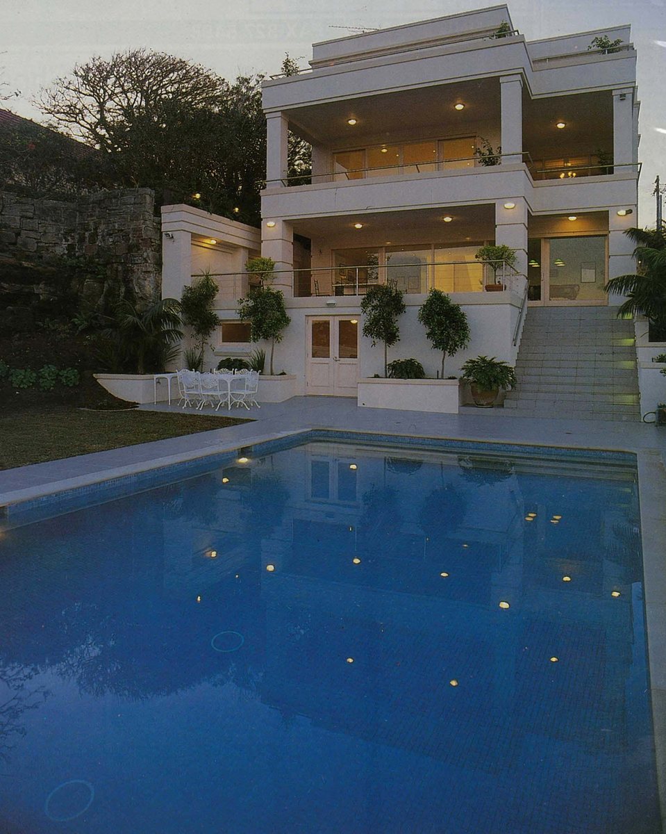 Bay Villa, a white multi-level waterfront residence with a lit pool at dusk