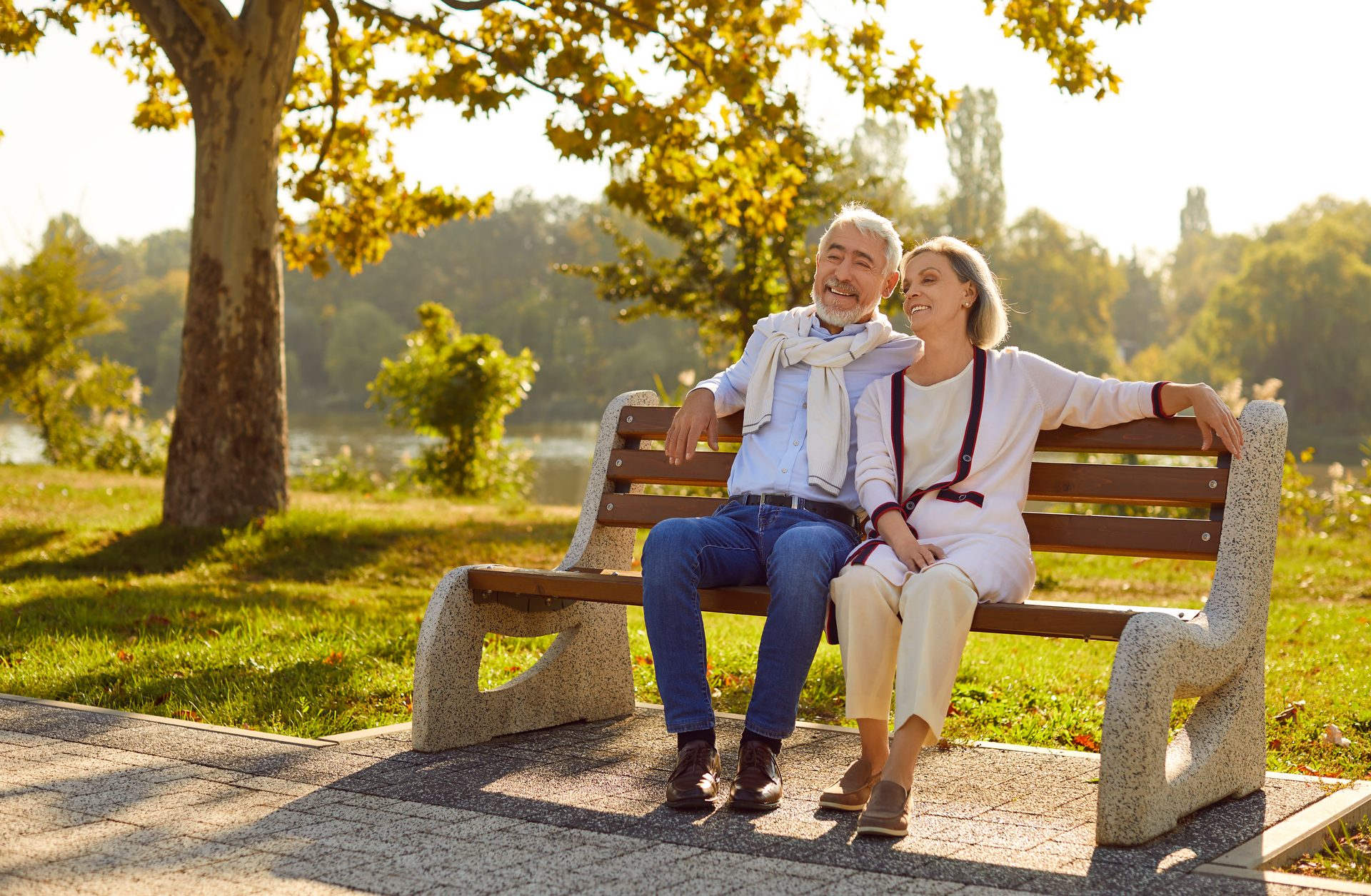 Smiling older couple relaxing together on a park bench in the afternoon sun